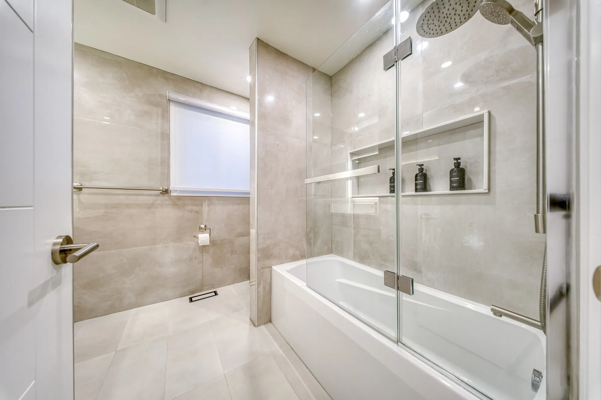 The finished bathroom: a tub behind glass in large grey tile.