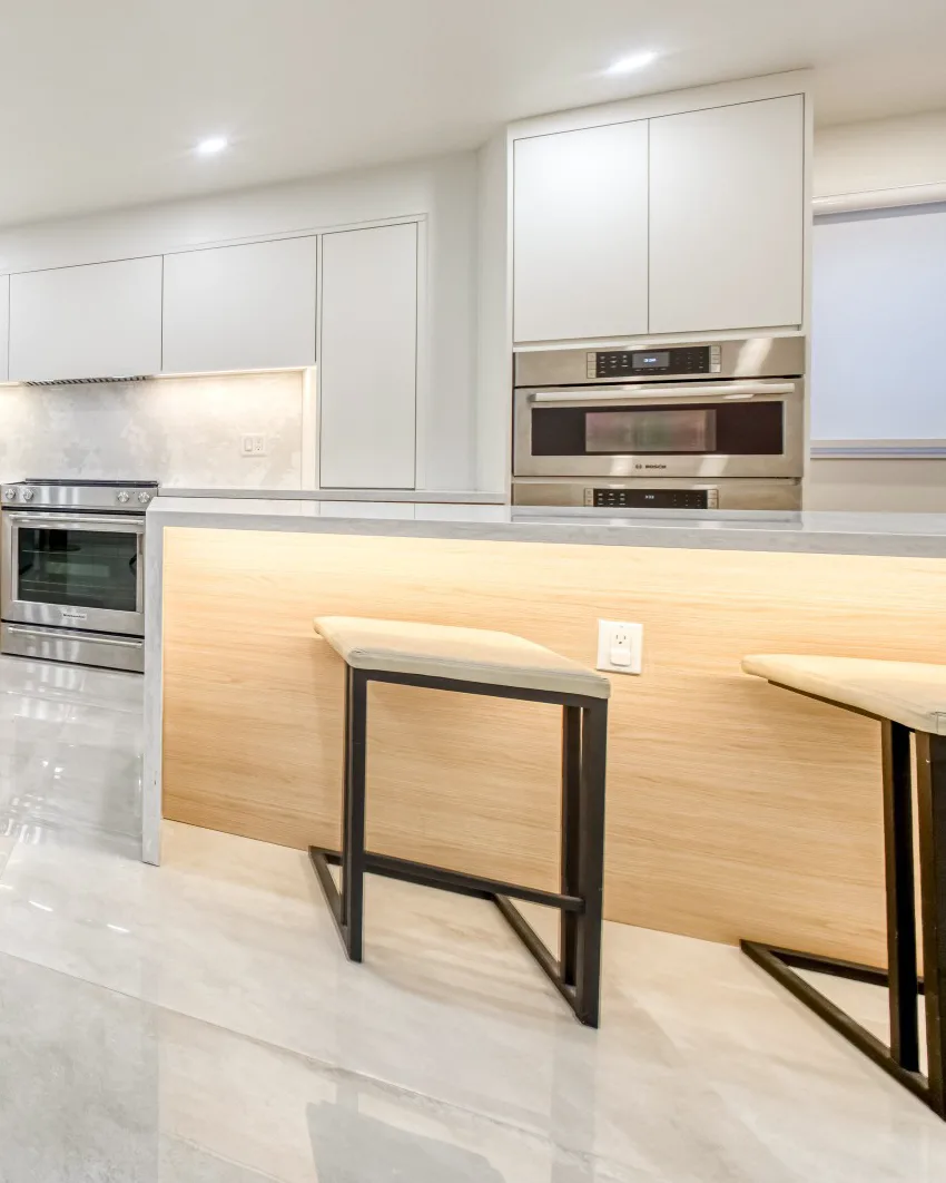 Wall ovens, an oak island lit from beneath and two stools on a stone floor.