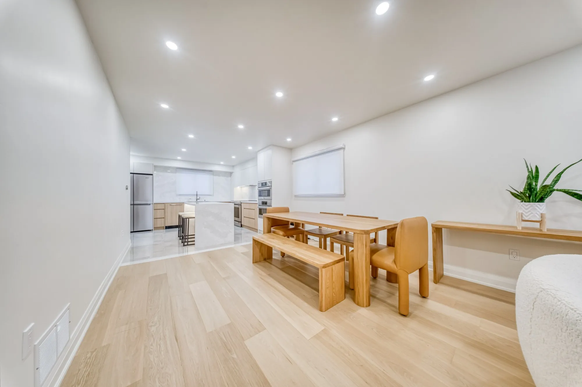 An oak dining table and bench on wide plank floors, with the kitchen beyond.