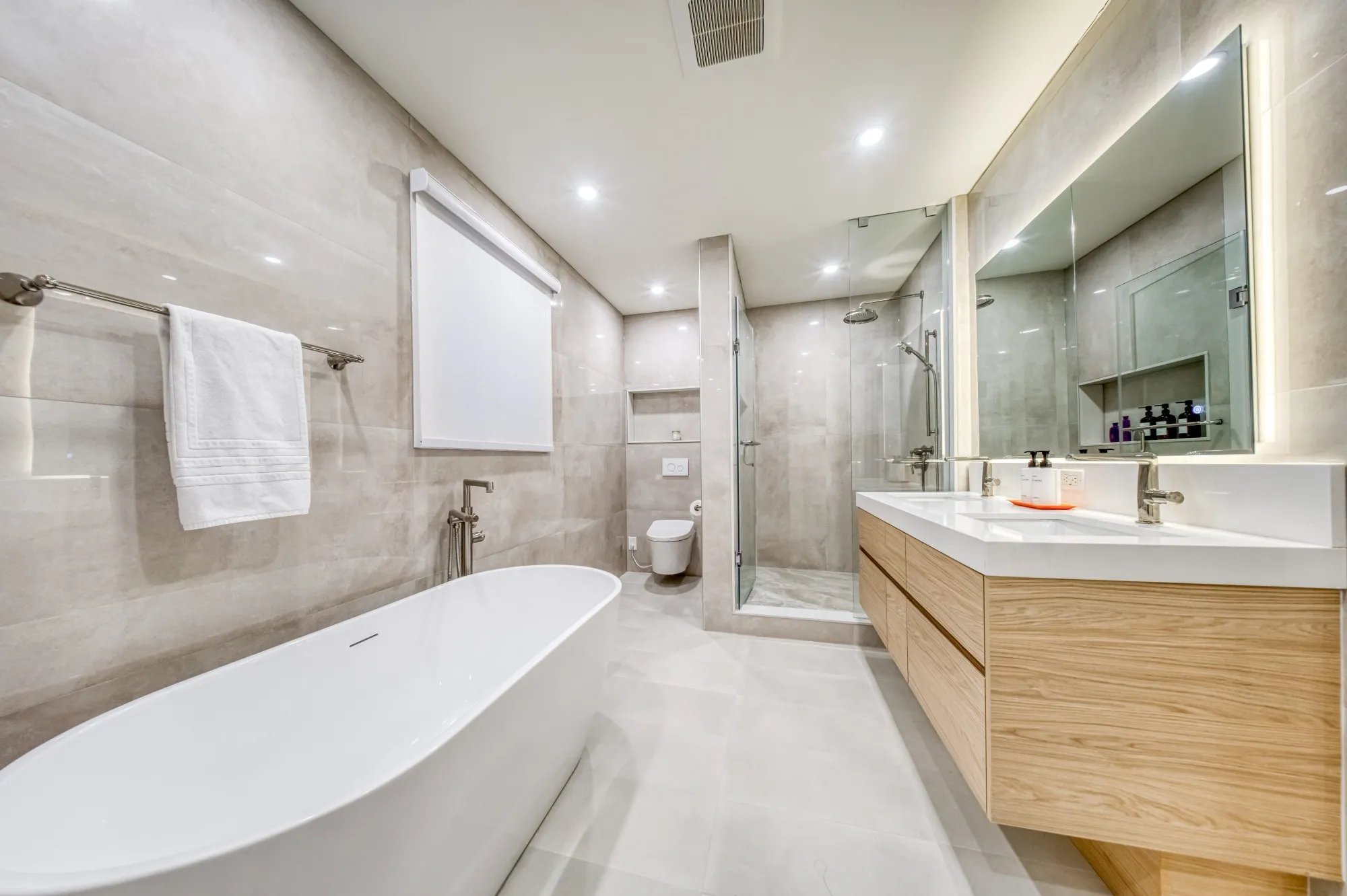 An ensuite with a freestanding tub, a floating oak double vanity and a glass shower in large grey tile.