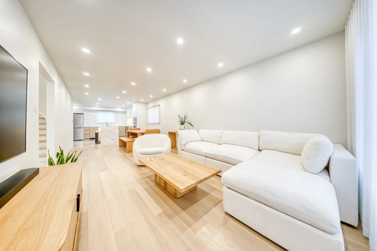 The living room: a cream sectional, a low oak table and a wall-mounted screen on plank floors.