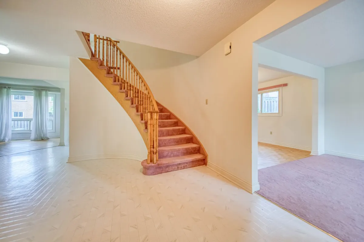 The entry before: a curved staircase with pink carpet and oak spindles.