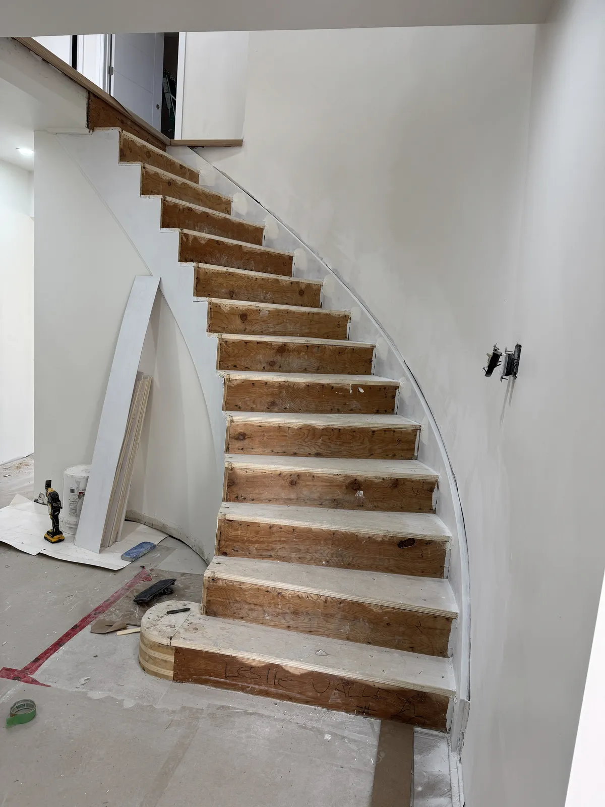 The staircase mid-renovation: carpet stripped to raw wooden treads and new drywall on the curve.